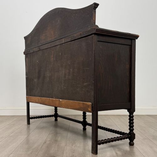 fig 6. A dark oak 19th-century sideboard featuring carved lion mask motifs, scrollwork panel doors, and bobbin-turned legs connected by stretchers.