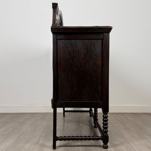 fig 7. A dark oak 19th-century sideboard featuring carved lion mask motifs, scrollwork panel doors, and bobbin-turned legs connected by stretchers.