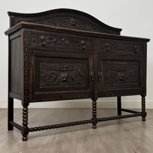 fig 8. A dark oak 19th-century sideboard featuring carved lion mask motifs, scrollwork panel doors, and bobbin-turned legs connected by stretchers.