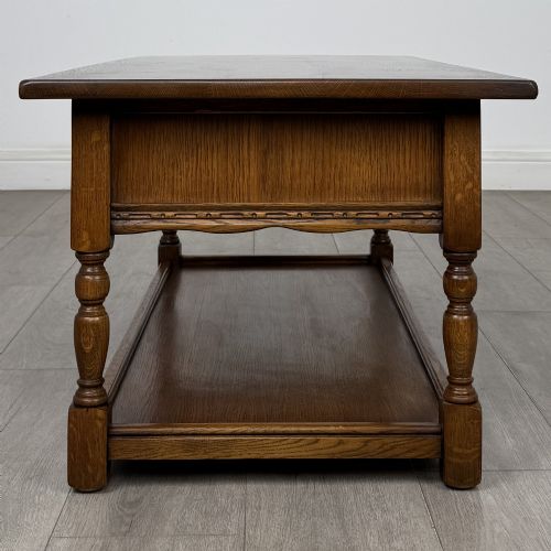 fig 2. A rectangular warm brown oak coffee table featuring two drawers with metal ring handles, carved apron detailing, turned legs, and a lower storage shelf.