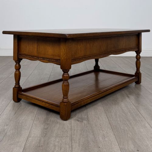 fig 3. A rectangular warm brown oak coffee table featuring two drawers with metal ring handles, carved apron detailing, turned legs, and a lower storage shelf.