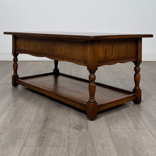 fig 5. A rectangular warm brown oak coffee table featuring two drawers with metal ring handles, carved apron detailing, turned legs, and a lower storage shelf.