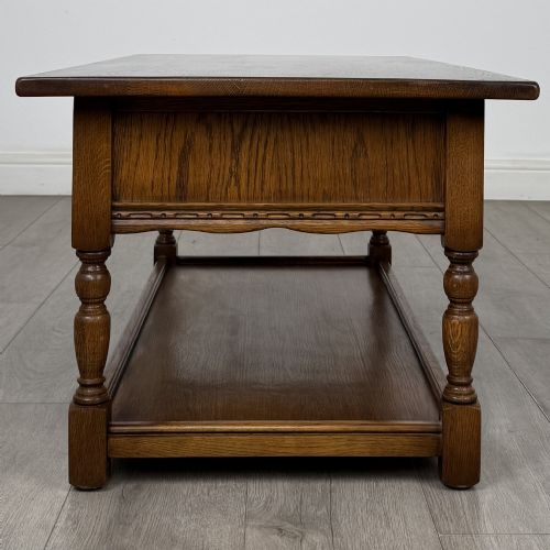 fig 6. A rectangular warm brown oak coffee table featuring two drawers with metal ring handles, carved apron detailing, turned legs, and a lower storage shelf.
