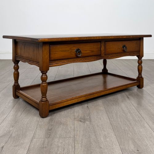 fig 7. A rectangular warm brown oak coffee table featuring two drawers with metal ring handles, carved apron detailing, turned legs, and a lower storage shelf.