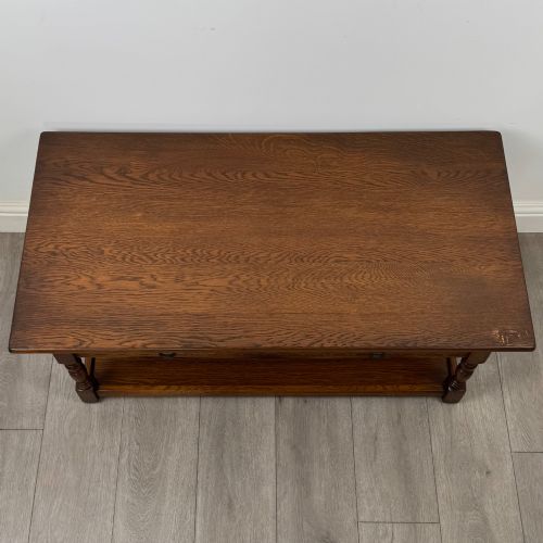 fig 8. A rectangular warm brown oak coffee table featuring two drawers with metal ring handles, carved apron detailing, turned legs, and a lower storage shelf.