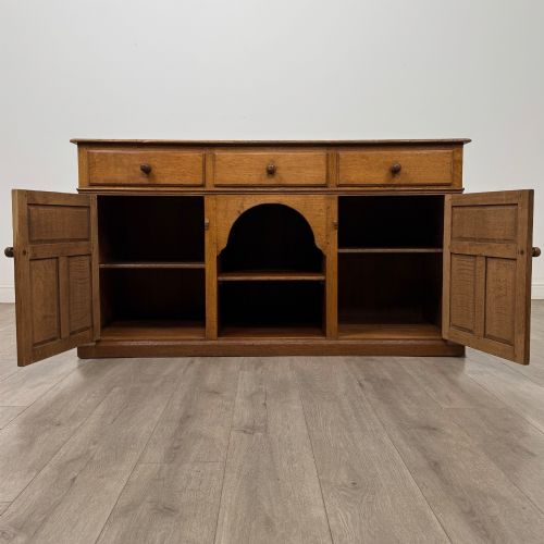 fig 1. An antique golden oak dresser base featuring three top drawers, two panelled outer doors, and a central arched open recess.