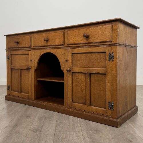 fig 2. An antique golden oak dresser base featuring three top drawers, two panelled outer doors, and a central arched open recess.