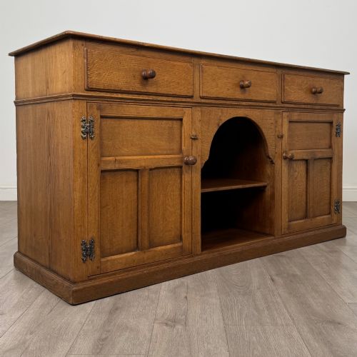 fig 8. An antique golden oak dresser base featuring three top drawers, two panelled outer doors, and a central arched open recess.