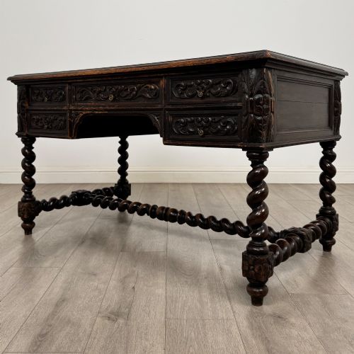 fig 1. A 19th-century dark oak writing table featuring carved drawer fronts, barley twist legs, and a low spiral stretcher.