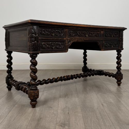 fig 7. A 19th-century dark oak writing table featuring carved drawer fronts, barley twist legs, and a low spiral stretcher.