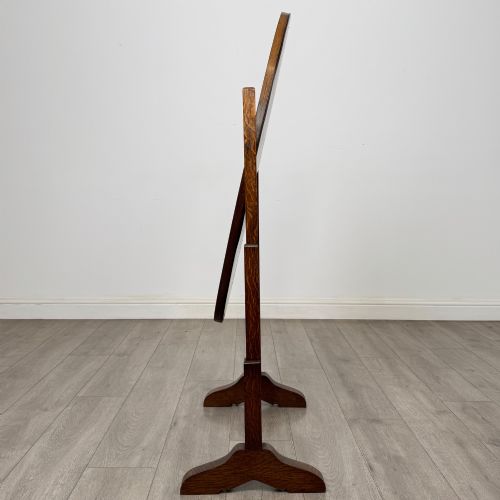 fig 1. An Edwardian oak cheval mirror featuring an oval glass frame suspended between two upright posts on trestle feet.
