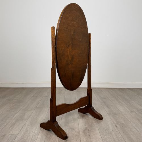 fig 2. An Edwardian oak cheval mirror featuring an oval glass frame suspended between two upright posts on trestle feet.