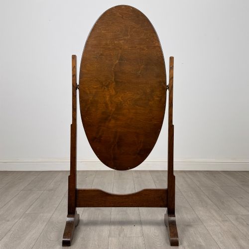 fig 3. An Edwardian oak cheval mirror featuring an oval glass frame suspended between two upright posts on trestle feet.