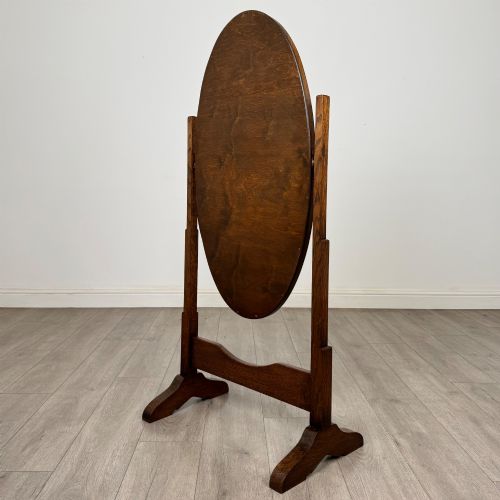 fig 4. An Edwardian oak cheval mirror featuring an oval glass frame suspended between two upright posts on trestle feet.