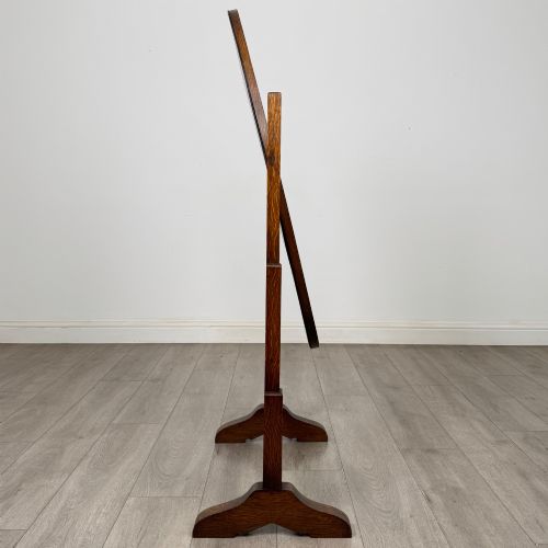 fig 5. An Edwardian oak cheval mirror featuring an oval glass frame suspended between two upright posts on trestle feet.