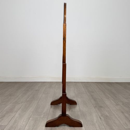 fig 6. An Edwardian oak cheval mirror featuring an oval glass frame suspended between two upright posts on trestle feet.