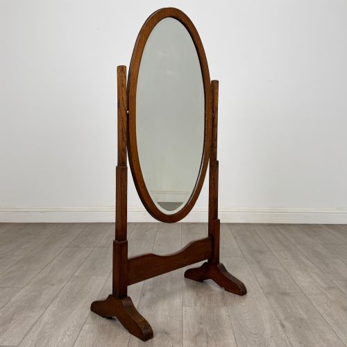 fig 7. An Edwardian oak cheval mirror featuring an oval glass frame suspended between two upright posts on trestle feet.