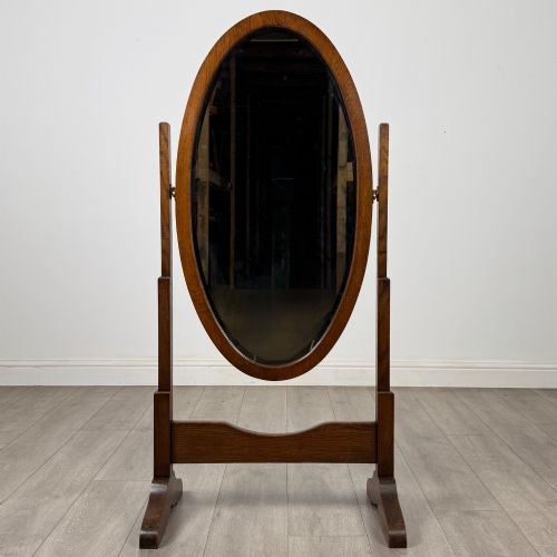 fig 8. An Edwardian oak cheval mirror featuring an oval glass frame suspended between two upright posts on trestle feet.