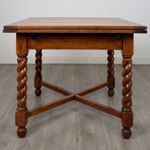 fig 3. An Edwardian warm oak draw leaf dining table featuring extended side leaves, barley twist legs, and an X-frame cross stretcher.