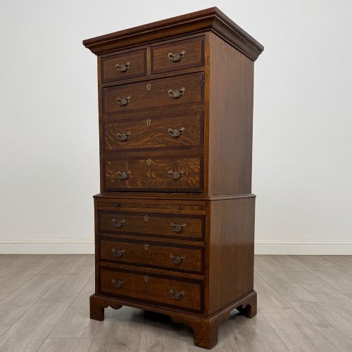 fig 2. A tall early 20th-century oak chest on chest featuring multiple drawers with crossbanded borders and brass drop handles set on bracket feet.