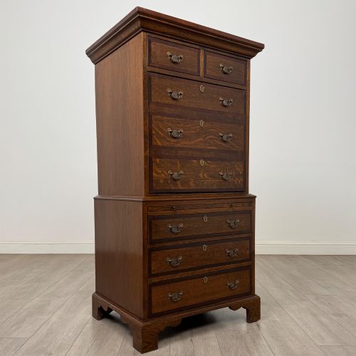 fig 8. A tall early 20th-century oak chest on chest featuring multiple drawers with crossbanded borders and brass drop handles set on bracket feet.