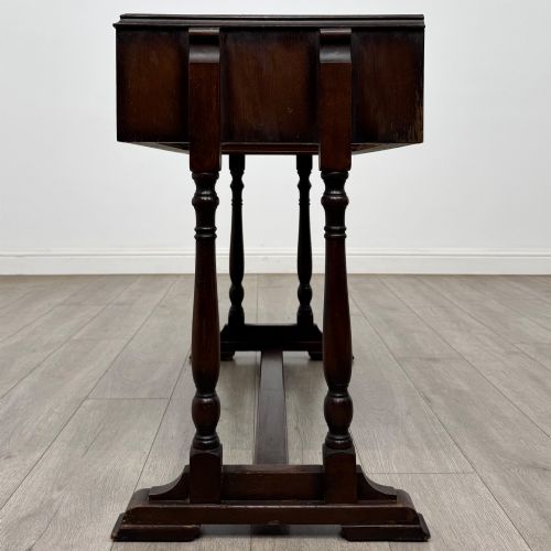 fig 2. A dark brown carved oak side table featuring two scroll-carved front drawers with metal drop handles and turned trestle legs.