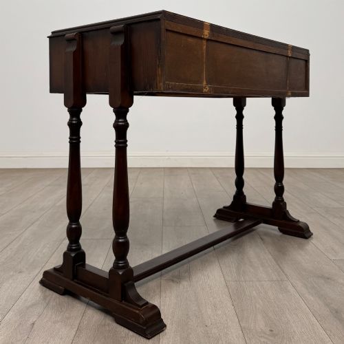 fig 3. A dark brown carved oak side table featuring two scroll-carved front drawers with metal drop handles and turned trestle legs.