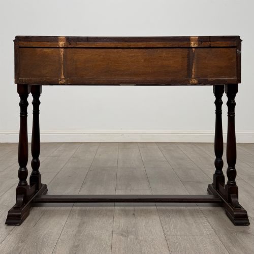 fig 4. A dark brown carved oak side table featuring two scroll-carved front drawers with metal drop handles and turned trestle legs.