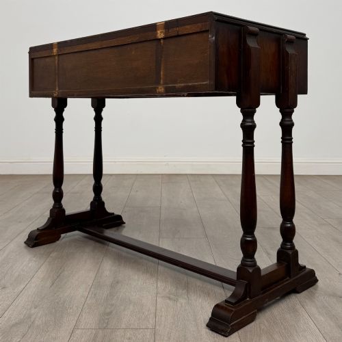 fig 5. A dark brown carved oak side table featuring two scroll-carved front drawers with metal drop handles and turned trestle legs.
