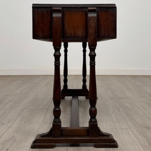 fig 6. A dark brown carved oak side table featuring two scroll-carved front drawers with metal drop handles and turned trestle legs.
