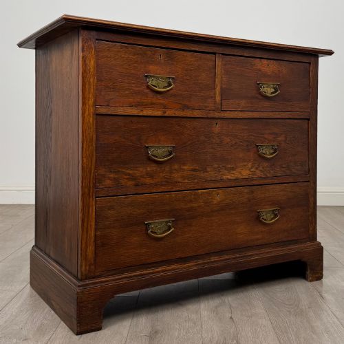 fig 7. An antique Edwardian dark oak chest of drawers featuring two small top drawers above two full-width drawers with brass handles.