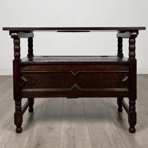 fig 1. A dark oak monks bench featuring a panelled backrest with a central diamond motif, turned arm supports, and a lift-up seat.
