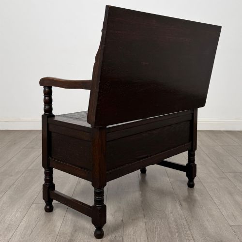 fig 4. A dark oak monks bench featuring a panelled backrest with a central diamond motif, turned arm supports, and a lift-up seat.