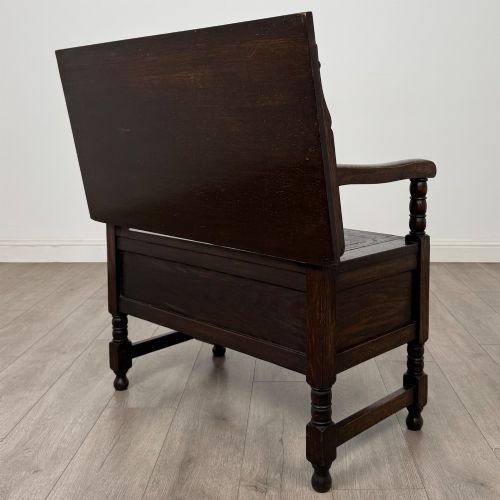 fig 6. A dark oak monks bench featuring a panelled backrest with a central diamond motif, turned arm supports, and a lift-up seat.