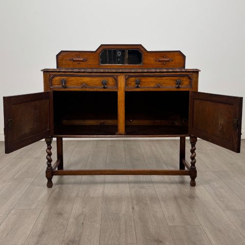 fig 1. An Edwardian golden oak sideboard featuring a raised mirror back gallery, two drawers, two cabinet doors with geometric mouldings, and barley twist front legs.