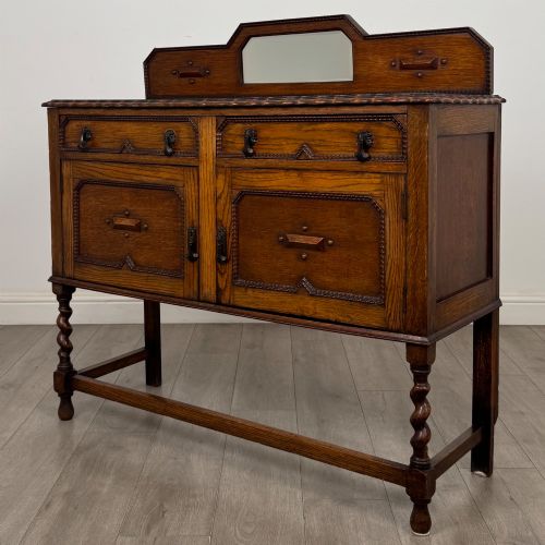 fig 2. An Edwardian golden oak sideboard featuring a raised mirror back gallery, two drawers, two cabinet doors with geometric mouldings, and barley twist front legs.