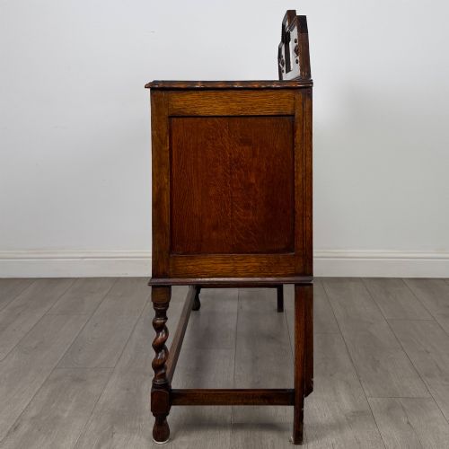 fig 3. An Edwardian golden oak sideboard featuring a raised mirror back gallery, two drawers, two cabinet doors with geometric mouldings, and barley twist front legs.