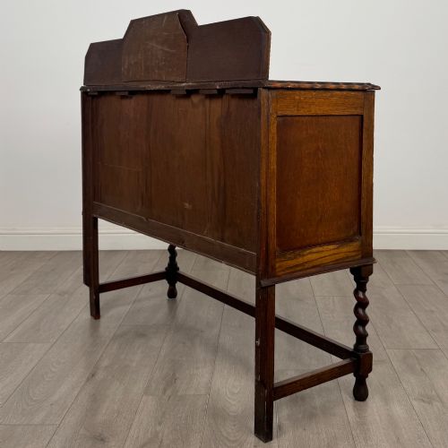 fig 6. An Edwardian golden oak sideboard featuring a raised mirror back gallery, two drawers, two cabinet doors with geometric mouldings, and barley twist front legs.