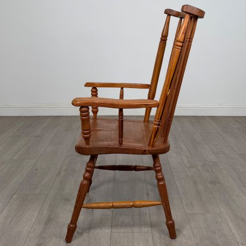 fig 1. A twentieth-century pitch pine armchair featuring a tall stick back, sculpted armrests, and turned legs joined by stretchers.