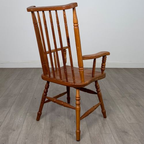 fig 4. A twentieth-century pitch pine armchair featuring a tall stick back, sculpted armrests, and turned legs joined by stretchers.