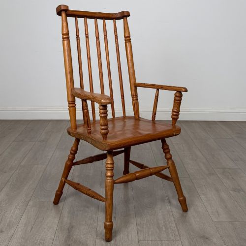 fig 6. A twentieth-century pitch pine armchair featuring a tall stick back, sculpted armrests, and turned legs joined by stretchers.