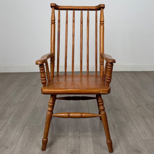 fig 7. A twentieth-century pitch pine armchair featuring a tall stick back, sculpted armrests, and turned legs joined by stretchers.
