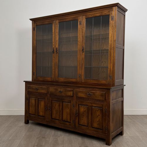 fig 2. A large dark oak display cabinet featuring three leaded glass doors above three drawers and three panelled cupboard doors.