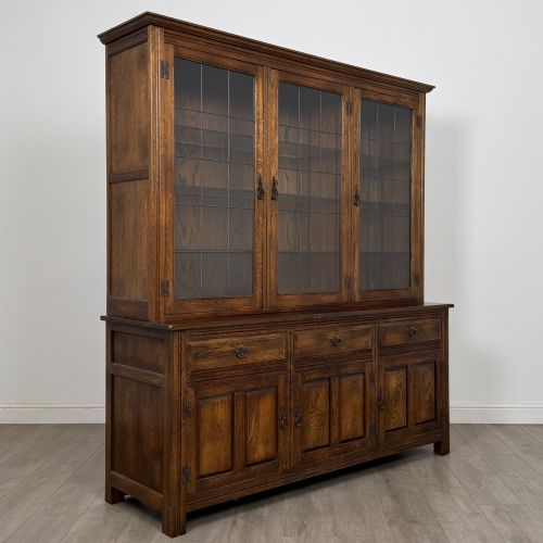 fig 8. A large dark oak display cabinet featuring three leaded glass doors above three drawers and three panelled cupboard doors.