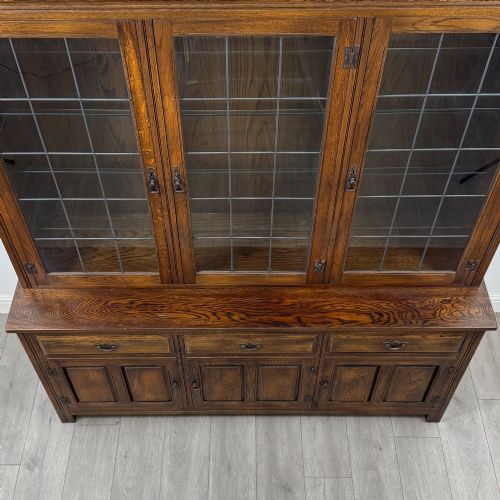 fig 9. A large dark oak display cabinet featuring three leaded glass doors above three drawers and three panelled cupboard doors.