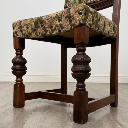 fig 5. A set of six dark oak dining chairs with carved crest rails, floral tapestry upholstered backrests and seats, and turned front legs.