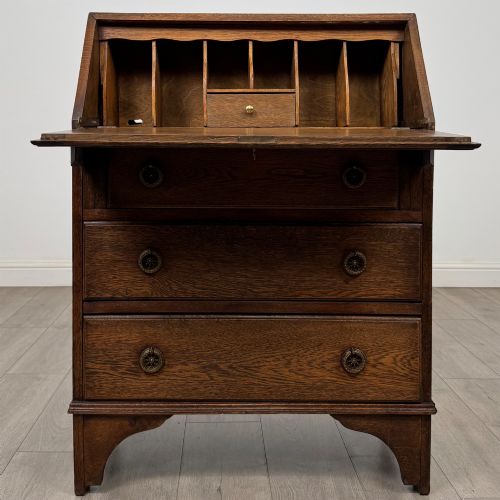 fig 1. An Edwardian oak bureau featuring a slanted fall-front lid above three drawers with decorative circular brass drop handles.