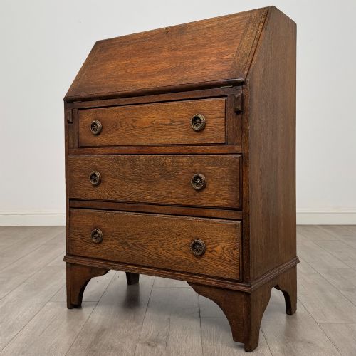 fig 2. An Edwardian oak bureau featuring a slanted fall-front lid above three drawers with decorative circular brass drop handles.