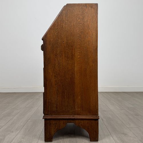 fig 3. An Edwardian oak bureau featuring a slanted fall-front lid above three drawers with decorative circular brass drop handles.