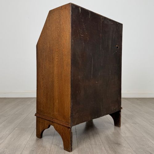 fig 4. An Edwardian oak bureau featuring a slanted fall-front lid above three drawers with decorative circular brass drop handles.